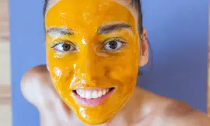 Uśmiechnięta twarz z maseczką z kurkumy, która rozjaśnia cerę. Naturalne piękno w domowym spa.