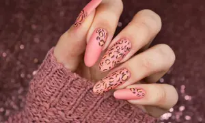 Długie, matowe paznokcie w kolorze brzoskwiniowym z motywem panterki. Wzory panterki są w odcieniach czerni i pomarańczu, tworząc efektowny manicure.