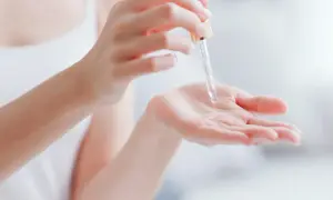 Kropla serum z pipetki spada na dłoń, pokazując, co to jest serum – skoncentrowany kosmetyk pielęgnacyjny.