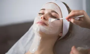 Kobieta z opaską na głowie otrzymuje peeling enzymatyczny nakładany pędzelkiem. Dowiedz się, jak stosować peeling enzymatyczny dla promiennej cery.