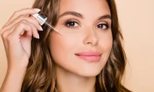 Kobieta aplikuje serum z pipetką na policzek, by poznać retinol działanie.