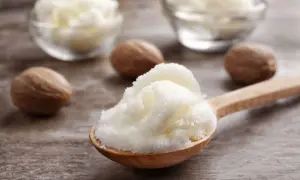 Łyżka z puszystym masłem shea, obok orzechy shea. Dowiedz się, co to masło shea i jakie ma właściwości.