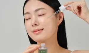 Kobieta z zamkniętymi oczami aplikuje serum do twarzy HE:ARIM CICA PANTHENOL AMPULE za pomocą pipety. To prosty sposób, jak stosować serum do twarzy dla promiennej cery.