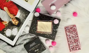 Złoty rozświetlacz Anastasia Beverly Hills na czarnym opakowaniu z gwiazdami, obok różowego etui i magazynu.