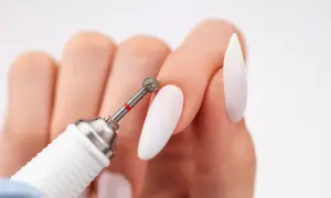 Zbliżenie na dłoń z białymi paznokciami i frezarką. Dowiedz się, jak włożyć frez do frezarki, by stworzyć idealny manicure.