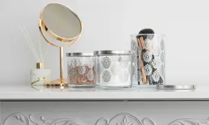 Elegancka organizacja kosmetyków: szklane pojemniki z ozdobnym wzorem, lusterko, patyczki zapachowe i pędzle do makijażu.