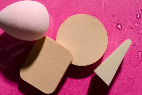 Różowy i beżowy beauty blender oraz gąbeczki na mokrym, fuksjowym tle. Dowiedz się, jak wyczyścić beauty blender, by służył Ci dłużej.