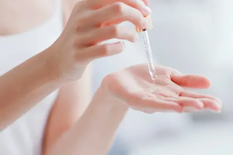 Kropla serum z pipetki spada na dłoń, pokazując, co to jest serum – skoncentrowany kosmetyk pielęgnacyjny.