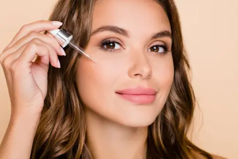 Kobieta aplikuje serum z pipetką na policzek, by poznać retinol działanie.