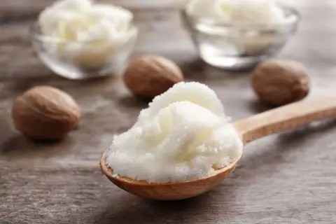 Łyżka z puszystym masłem shea, obok orzechy shea. Dowiedz się, co to masło shea i jakie ma właściwości.