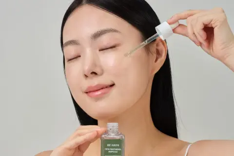 Kobieta z zamkniętymi oczami aplikuje serum do twarzy HE:ARIM CICA PANTHENOL AMPULE za pomocą pipety. To prosty sposób, jak stosować serum do twarzy dla promiennej cery.