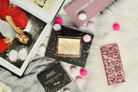Złoty rozświetlacz Anastasia Beverly Hills na czarnym opakowaniu z gwiazdami, obok różowego etui i magazynu.