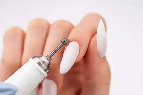 Zbliżenie na dłoń z białymi paznokciami i frezarką. Dowiedz się, jak włożyć frez do frezarki, by stworzyć idealny manicure.