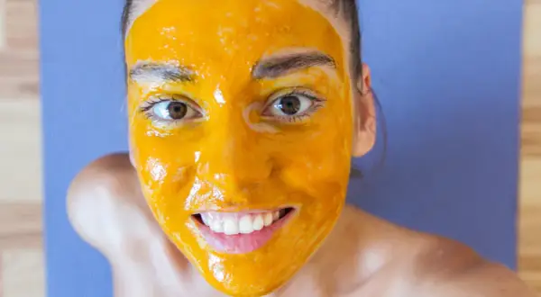 Uśmiechnięta twarz z maseczką z kurkumy, która rozjaśnia cerę. Naturalne piękno w domowym spa.