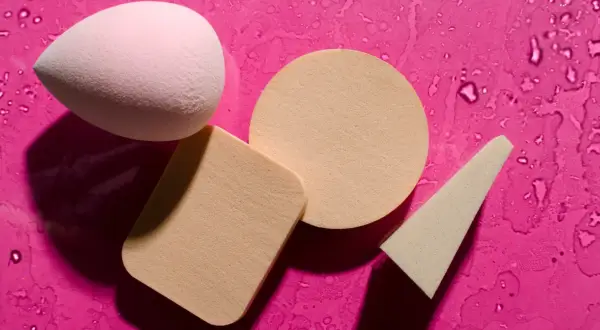 Różowy i beżowy beauty blender oraz gąbeczki na mokrym, fuksjowym tle. Dowiedz się, jak wyczyścić beauty blender, by służył Ci dłużej.