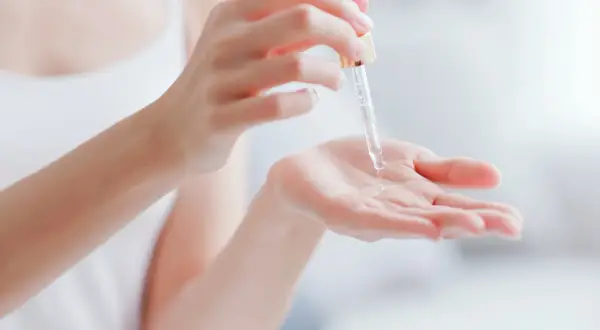 Kropla serum z pipetki spada na dłoń, pokazując, co to jest serum – skoncentrowany kosmetyk pielęgnacyjny.
