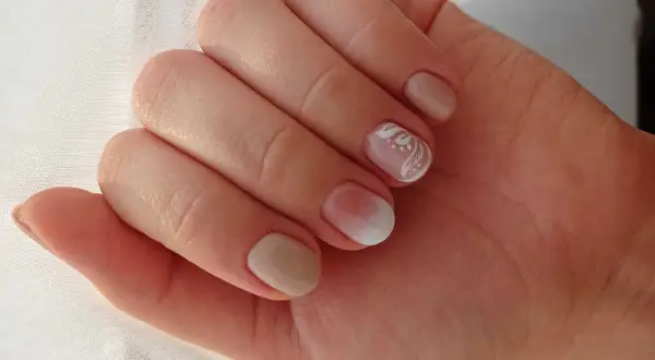 Delikatne rodzaje manicure: beżowe paznokcie z subtelnym zdobieniem białym wzorem na jednym paznokciu.