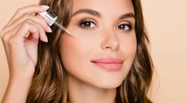 Kobieta aplikuje serum z pipetką na policzek, by poznać retinol działanie.