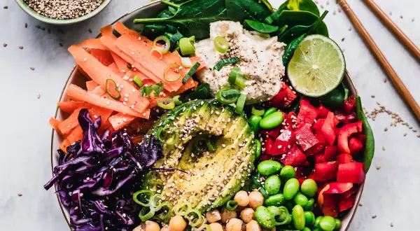 Kolorowa miska pełna warzyw: marchewka, awokado, czerwona kapusta, papryka, edamame, ciecierzyca i szpinak. To idealny posiłek dla nawilżenie skóry od środka.