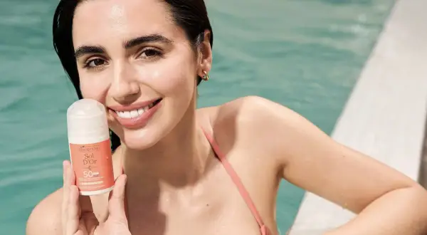 Uśmiechnięta kobieta w basenie trzyma krem z filtrem SPF 50. Oznacza to bardzo wysoką ochronę przed słońcem, idealną na wakacje.
