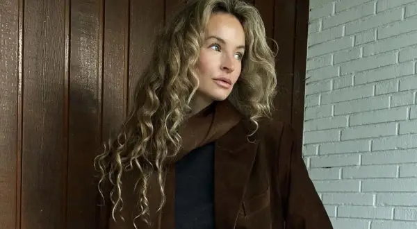 Kobieta z kręconymi blond włosami w brązowej marynarce. Kolor marynarki przypomina mi miód, taki **honey beige jaki to kolor** – ciepły i przytulny.