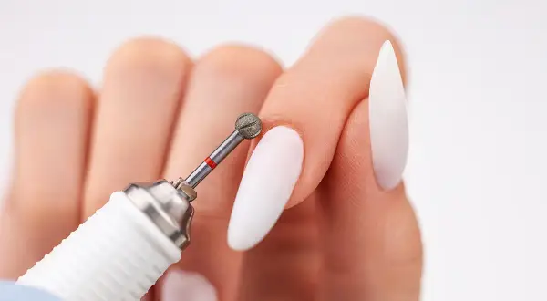 Zbliżenie na dłoń z białymi paznokciami i frezarką. Dowiedz się, jak włożyć frez do frezarki, by stworzyć idealny manicure.