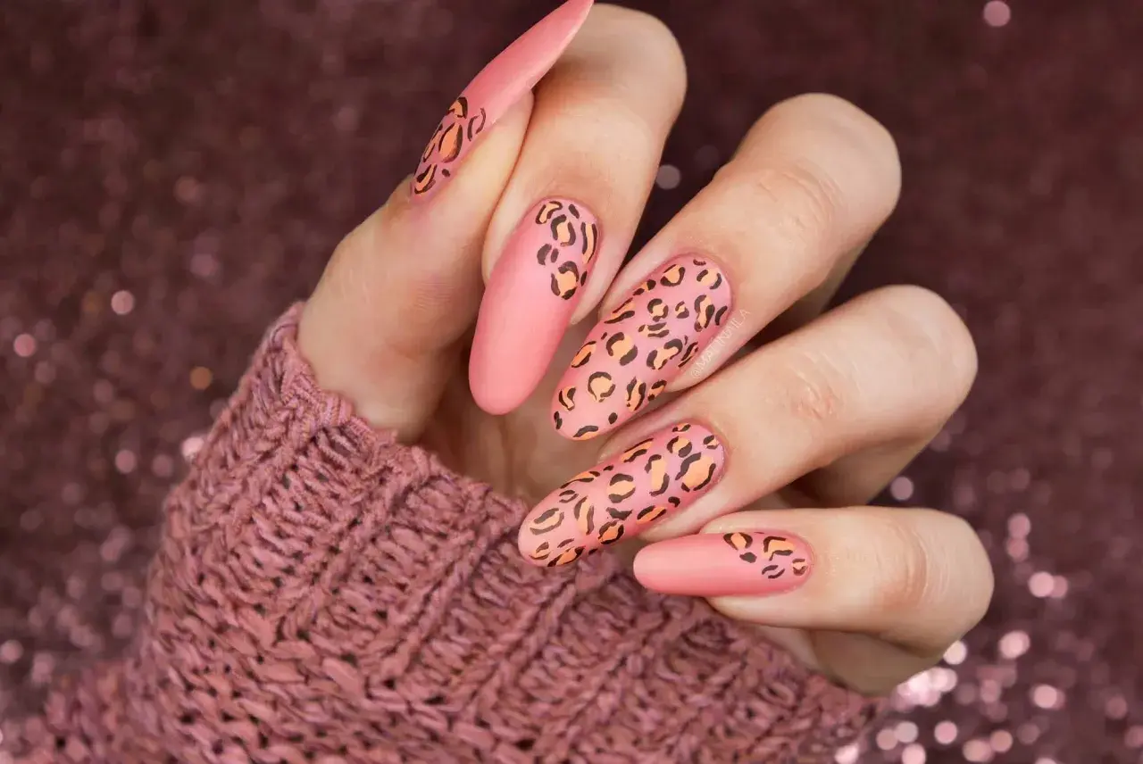 Długie, matowe paznokcie w kolorze brzoskwiniowym z motywem panterki. Wzory panterki są w odcieniach czerni i pomarańczu, tworząc efektowny manicure.