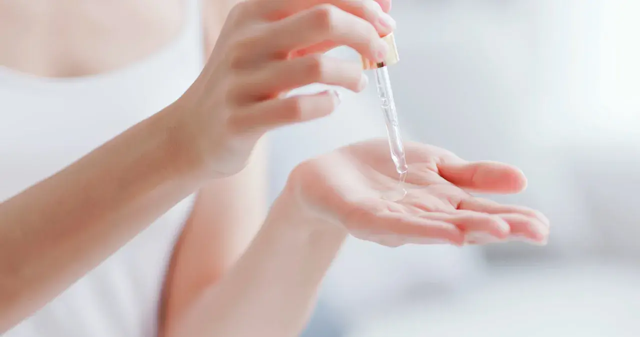Kropla serum z pipetki spada na dłoń, pokazując, co to jest serum – skoncentrowany kosmetyk pielęgnacyjny.