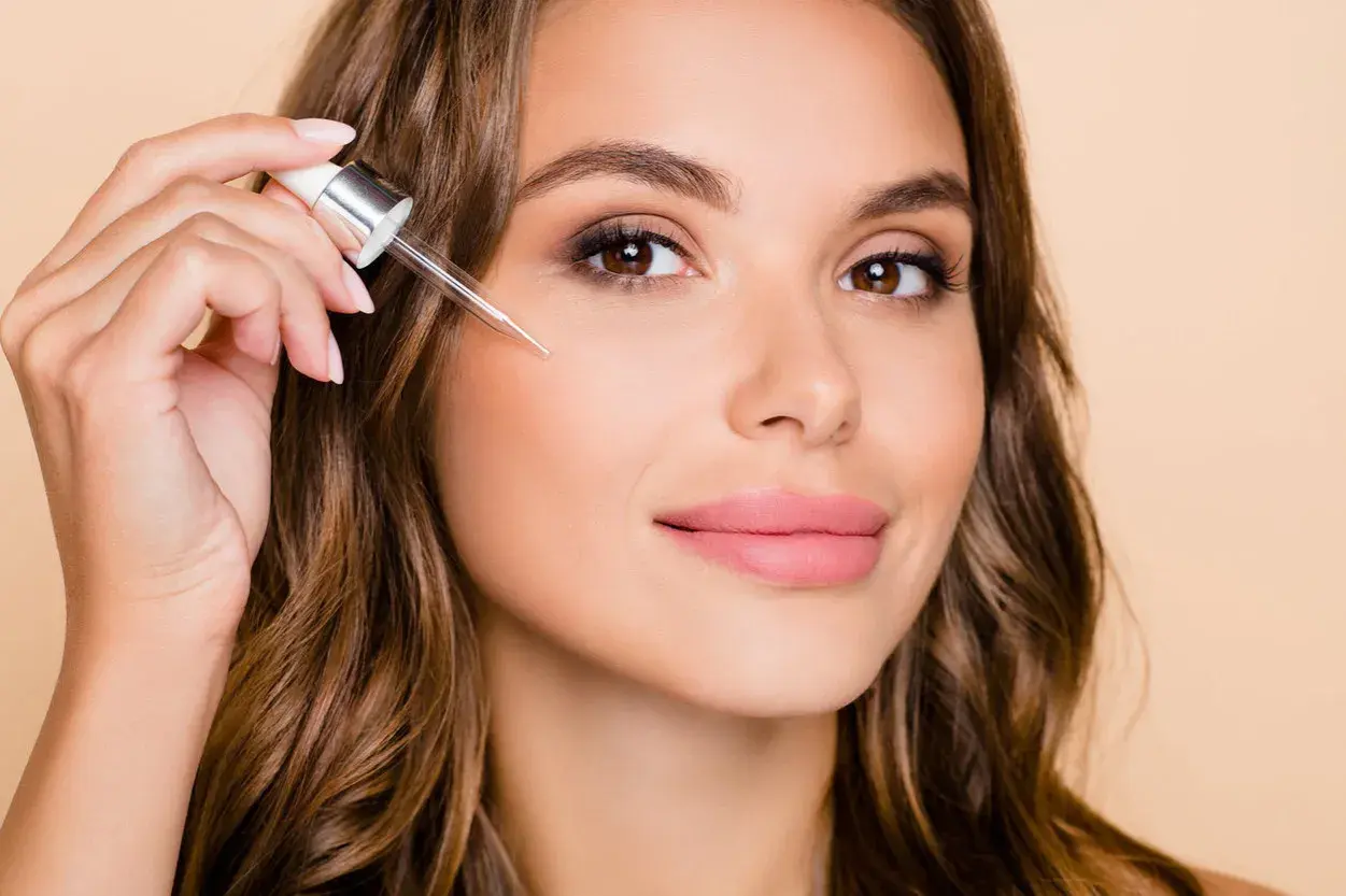 Kobieta aplikuje serum z pipetką na policzek, by poznać retinol działanie.