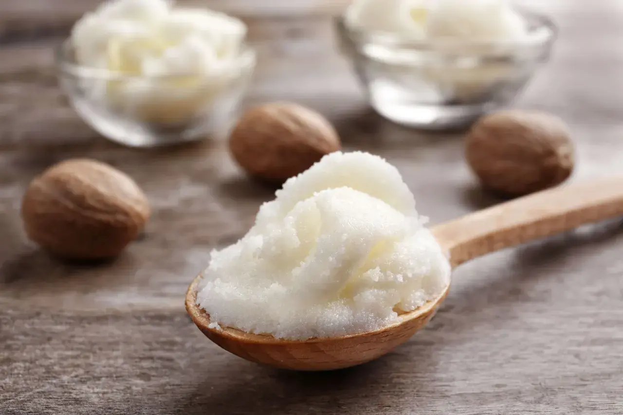 Łyżka z puszystym masłem shea, obok orzechy shea. Dowiedz się, co to masło shea i jakie ma właściwości.