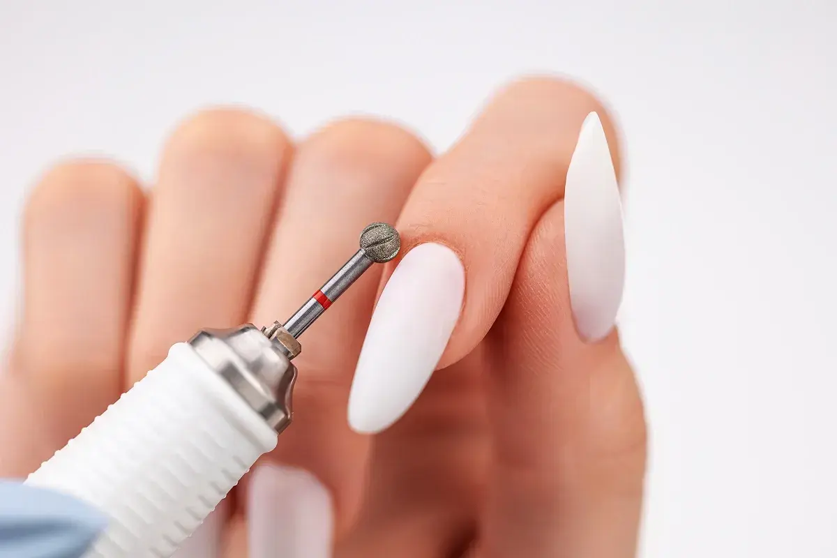 Zbliżenie na dłoń z białymi paznokciami i frezarką. Dowiedz się, jak włożyć frez do frezarki, by stworzyć idealny manicure.