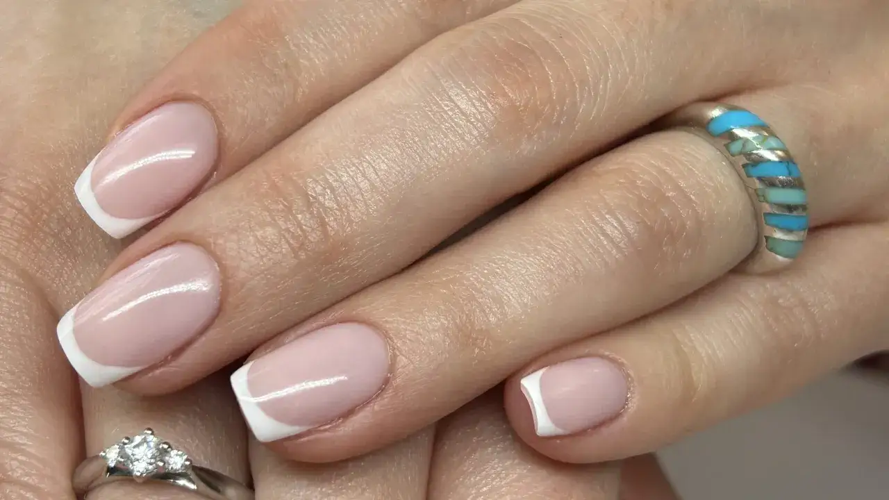 Elegancki manicure francuski na zadbanych dłoniach z pierścionkami. To kwintesencja klasyki i dbałości o detale.