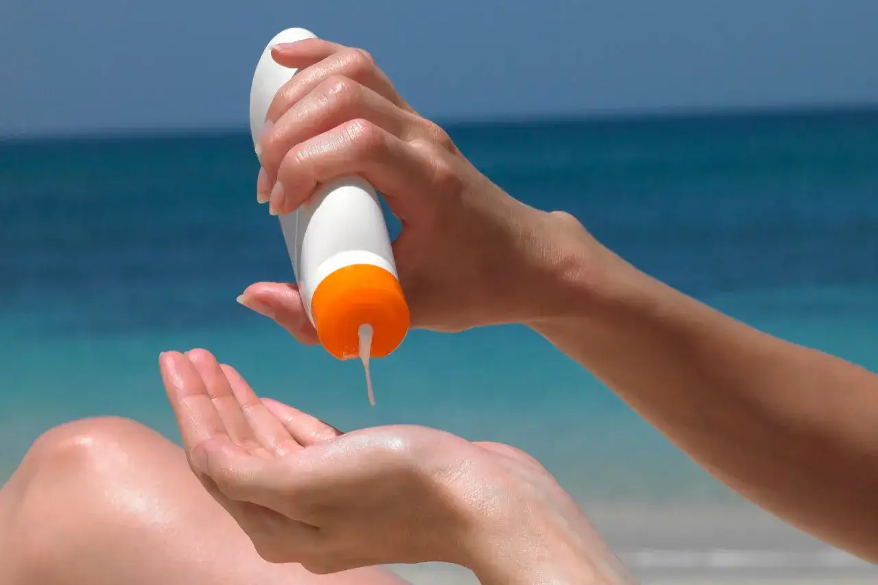 Dłoń aplikuje krem z filtrem SPF 50 na drugą dłoń. Wysoki wskaźnik ochrony przeciwsłonecznej zapewnia bezpieczeństwo na plaży.