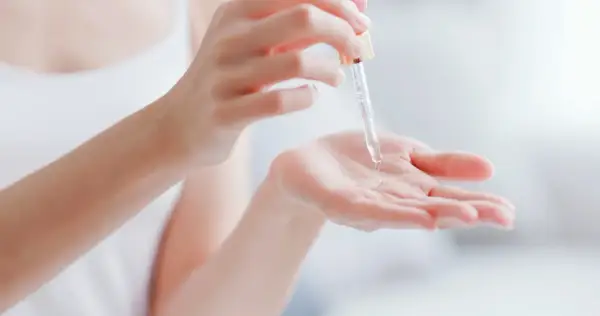Kropla serum z pipetki spada na dłoń, pokazując, co to jest serum – skoncentrowany kosmetyk pielęgnacyjny.