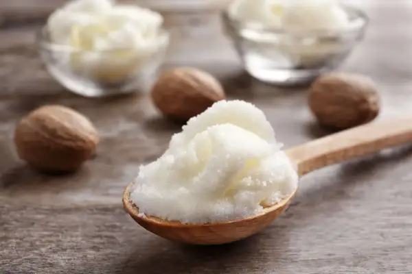 Łyżka z puszystym masłem shea, obok orzechy shea. Dowiedz się, co to masło shea i jakie ma właściwości.