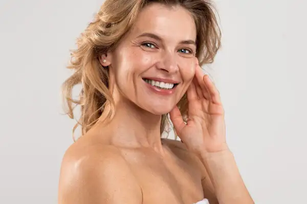 Uśmiechnięta kobieta z blond włosami, pokazująca swoją skórę. Odkryj domowe sposoby na zmarszczki i ciesz się piękną cerą.