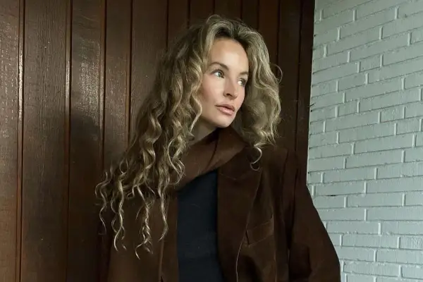 Kobieta z kręconymi blond włosami w brązowej marynarce. Kolor marynarki przypomina mi miód, taki **honey beige jaki to kolor** – ciepły i przytulny.