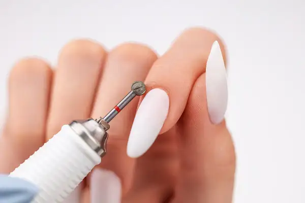 Zbliżenie na dłoń z białymi paznokciami i frezarką. Dowiedz się, jak włożyć frez do frezarki, by stworzyć idealny manicure.